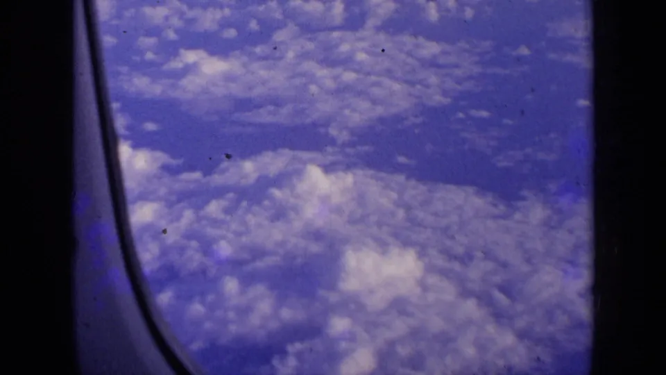 A passenger-window view shows blue sky and scattered clouds during the flight sequence.