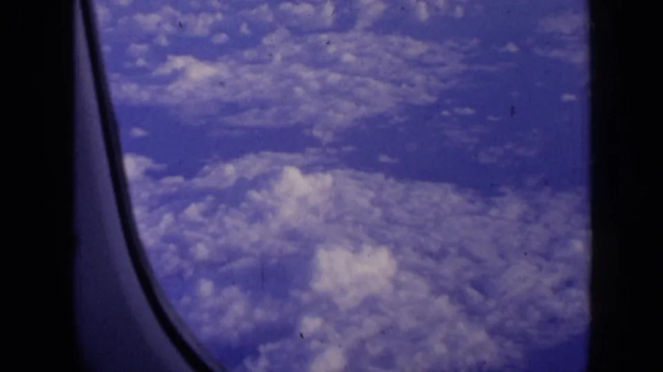 A soft 8mm passenger-window shot shows clouds and sky framed by the aircraft window.