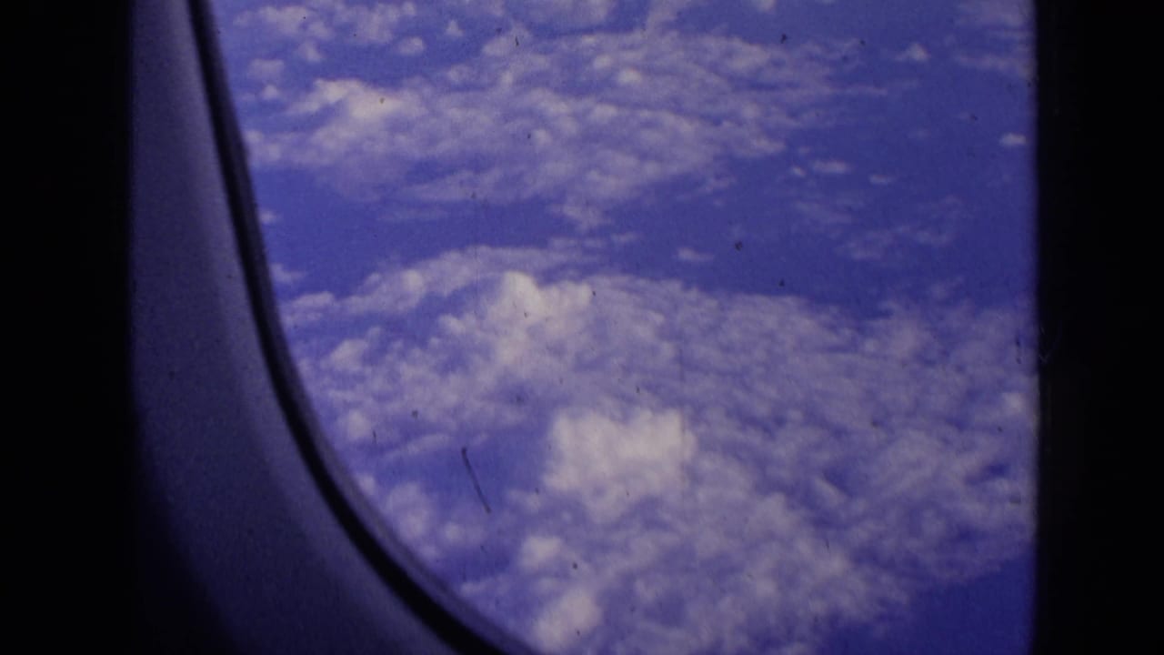 Cloud fields and blue sky framed by the airplane window edge.