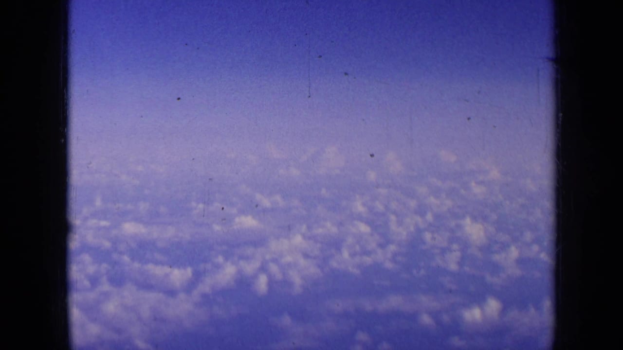 Blue sky and clouds seen through a dark airplane window frame.