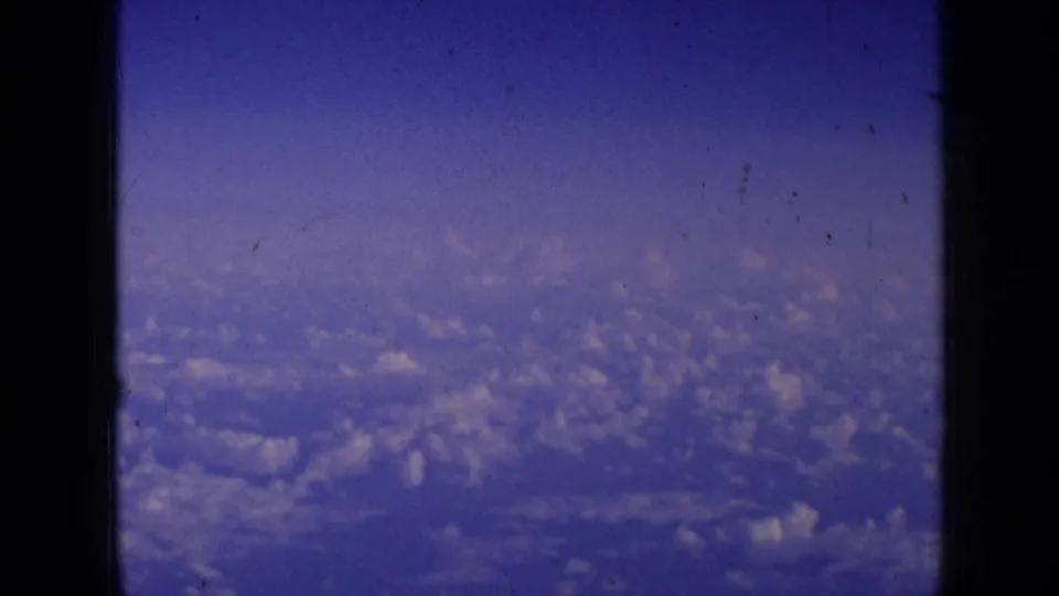 1963 8mm home-movie frame showing blue sky and cloud cover through the lower portion of an aircraft window.