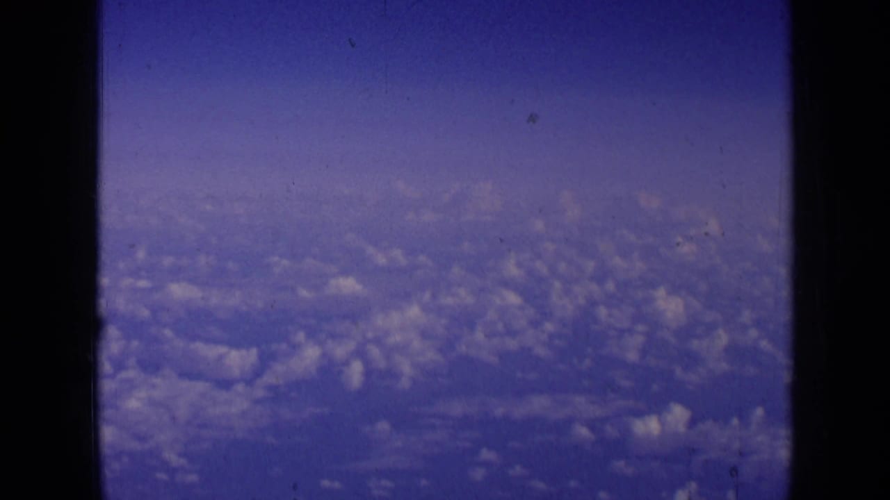 Blue sky and cloud tops seen through dark aircraft window edges.
