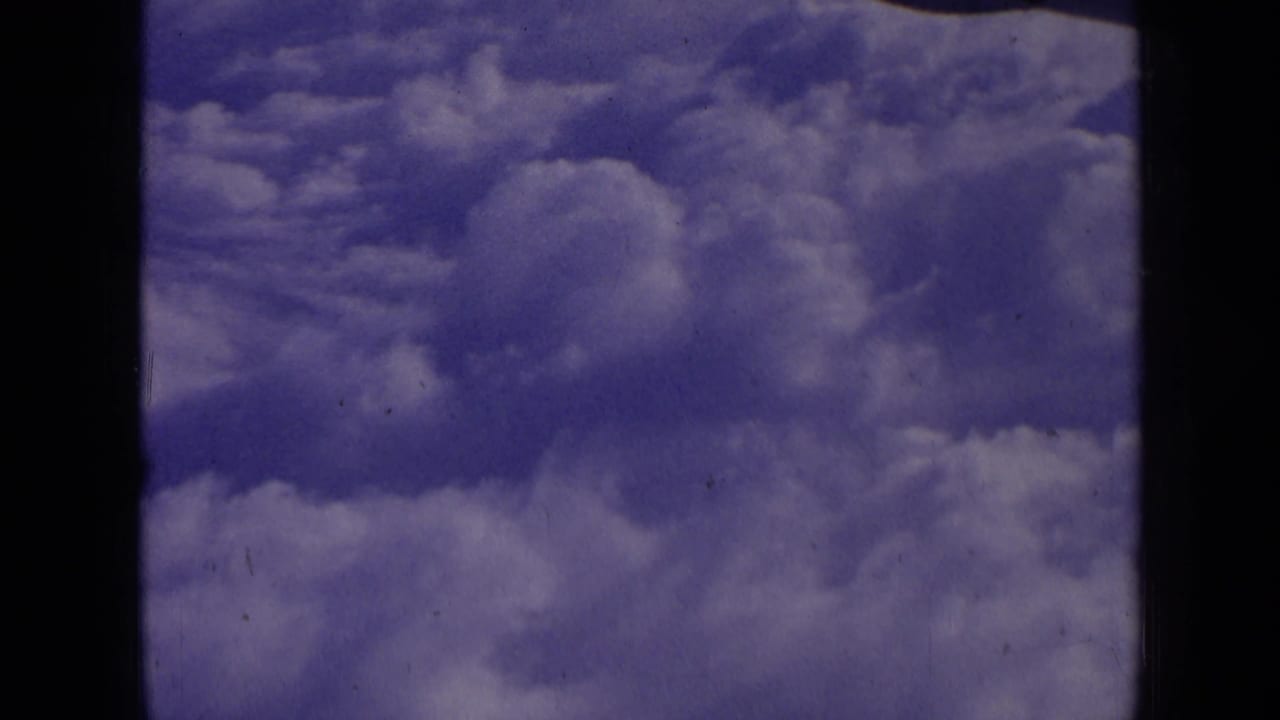 1963 8mm home-movie frame showing layered white clouds against a blue-purple sky, with visible film edge and grain.