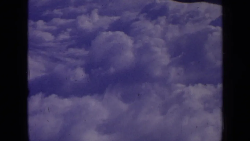 1963 8mm home-movie frame showing layered white clouds against a blue-purple sky, with visible film edge and grain.