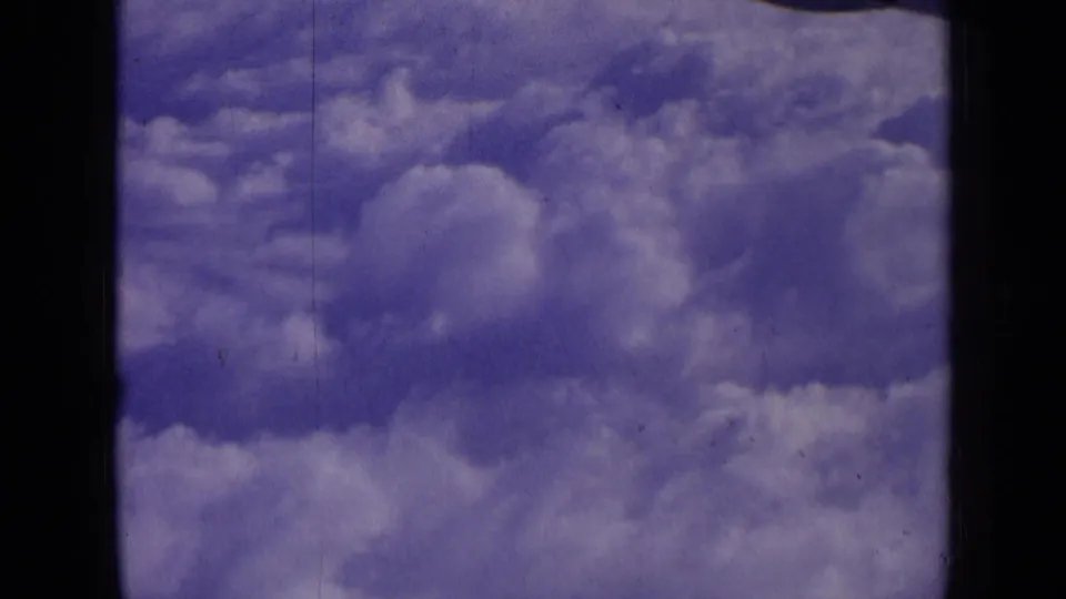 1963 8mm frame of bright cloud layers and hazy sky, with grain, scratches, and dark gate edges from the film scan.