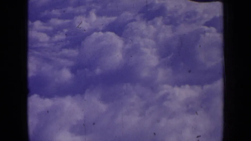 Final frame from the 1963 airplane cloud view, showing white clouds, blue-purple sky, and visible 8mm film wear.