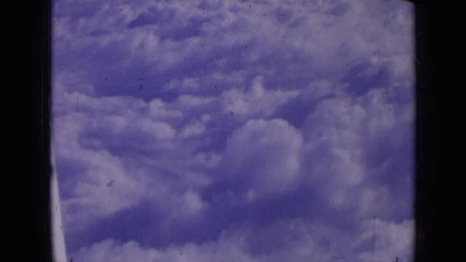 1963 8mm cloudscape with a soft cloud bank, blue-purple sky, grain, and the dark border of the original film frame.