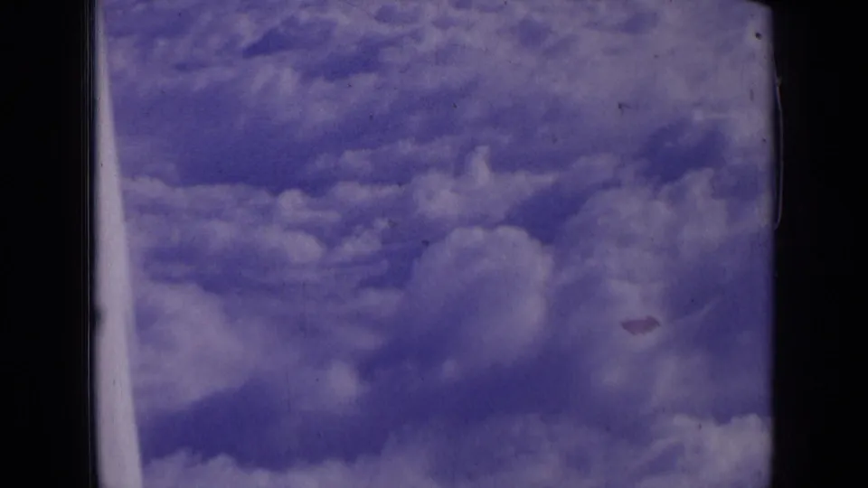 1963 8mm aerial view of clouds in blue-purple sky, with dark film borders and small dust marks visible in the scan.
