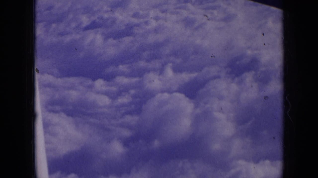 Cumulus clouds seen through a dark airplane window frame.