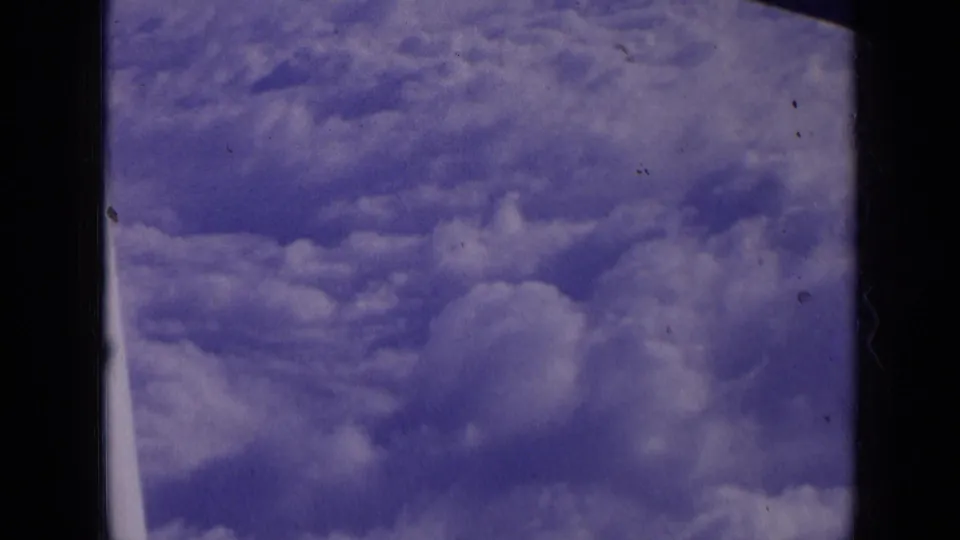 1963 8mm airplane-window view of layered cumulus clouds beneath a blue sky, with no ground detail visible.