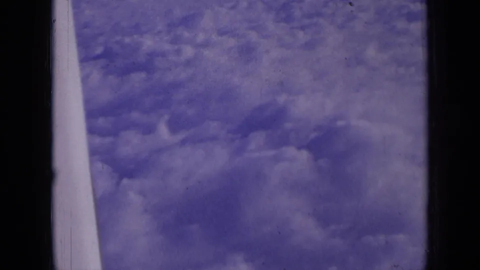 Airplane-window view of dense cumulus clouds under blue sky, recorded on 1963 8mm home-movie film.