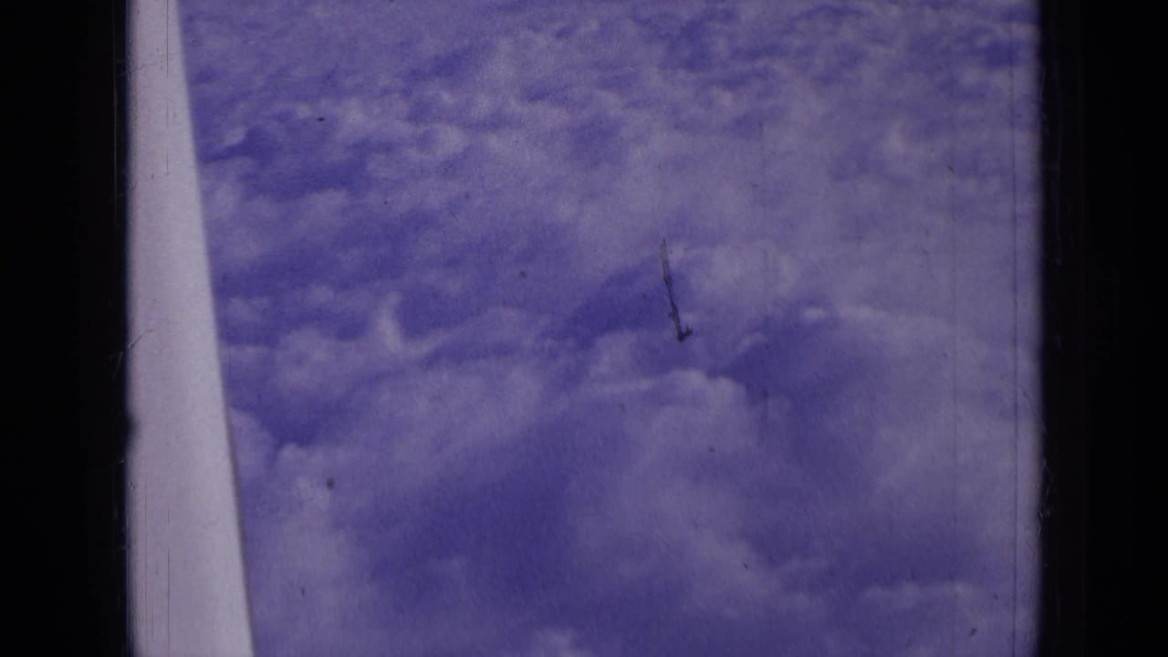 Clouds seen through an airplane window with a pale wing or strut at the left edge.