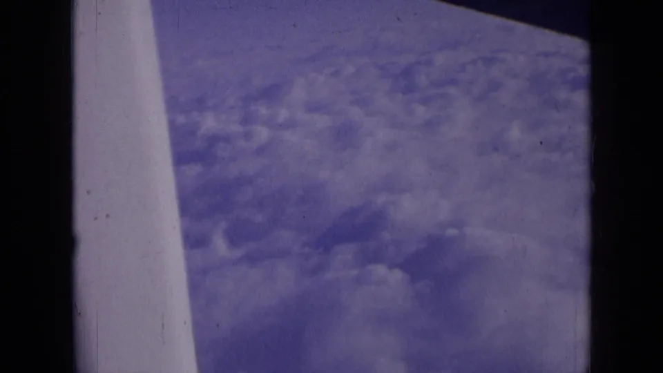 Purple-shifted 8mm airplane-window view over clouds, with a pale wing or strut along the left side.