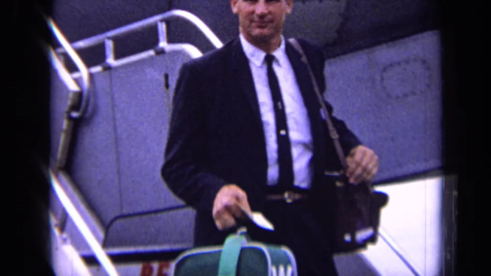 The suited passenger smiles while descending aircraft stairs at the London airport location supplied in the metadata.
