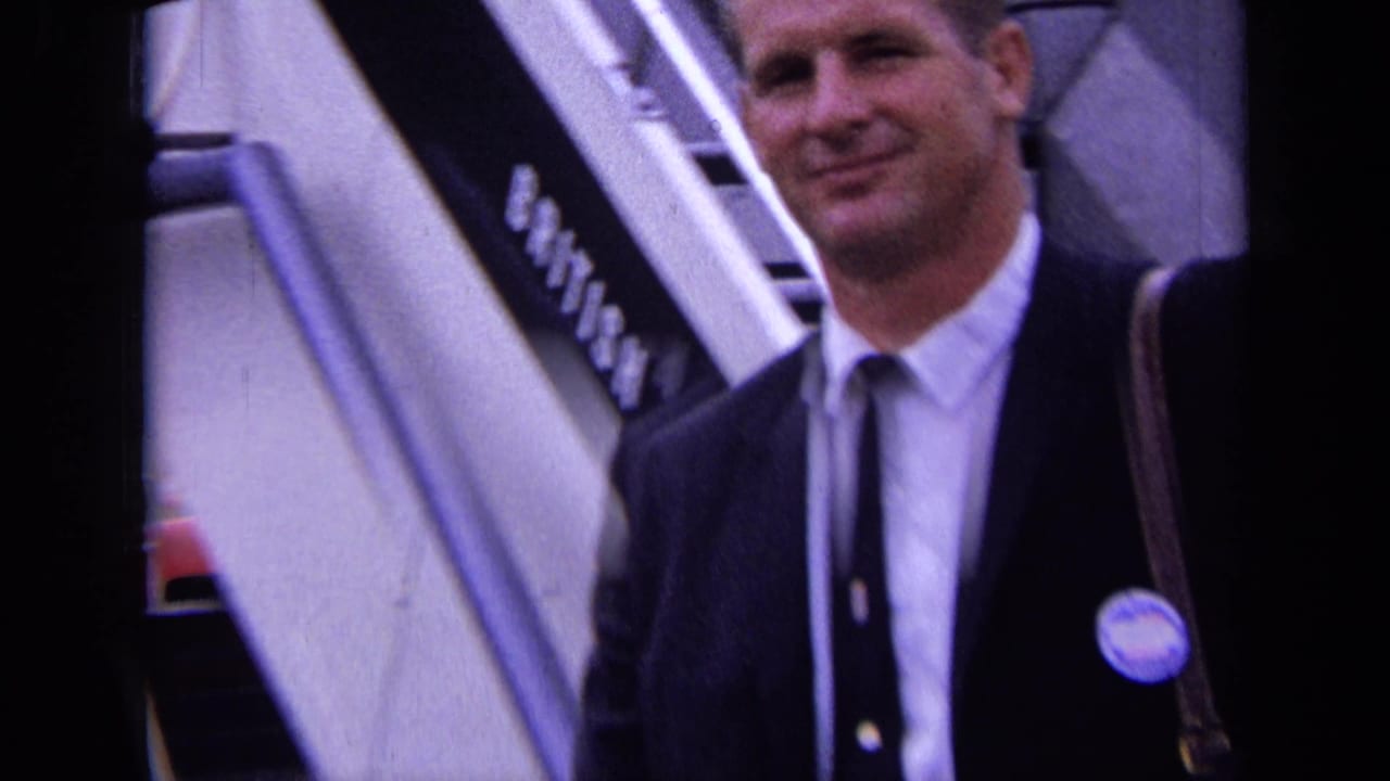 Suited man close to camera beside aircraft stairs on an airport tarmac.