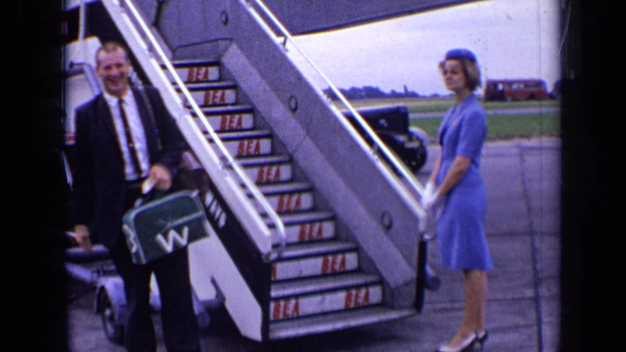 Suited man with briefcase stands near BEA aircraft stairs as a flight attendant waits nearby.