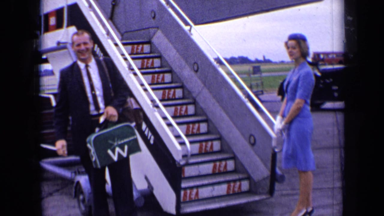 A suited passenger smiles near BEA aircraft stairs at a London airport, with a blue-uniformed attendant waiting to the side.