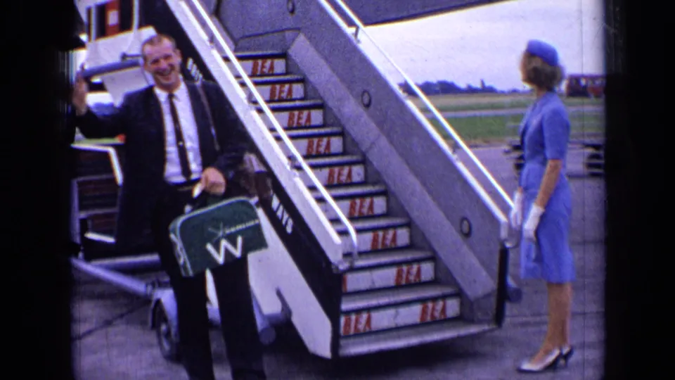 At the end of the clip, the suited passenger waves near BEA aircraft stairs as the attendant in blue faces the stairway.
