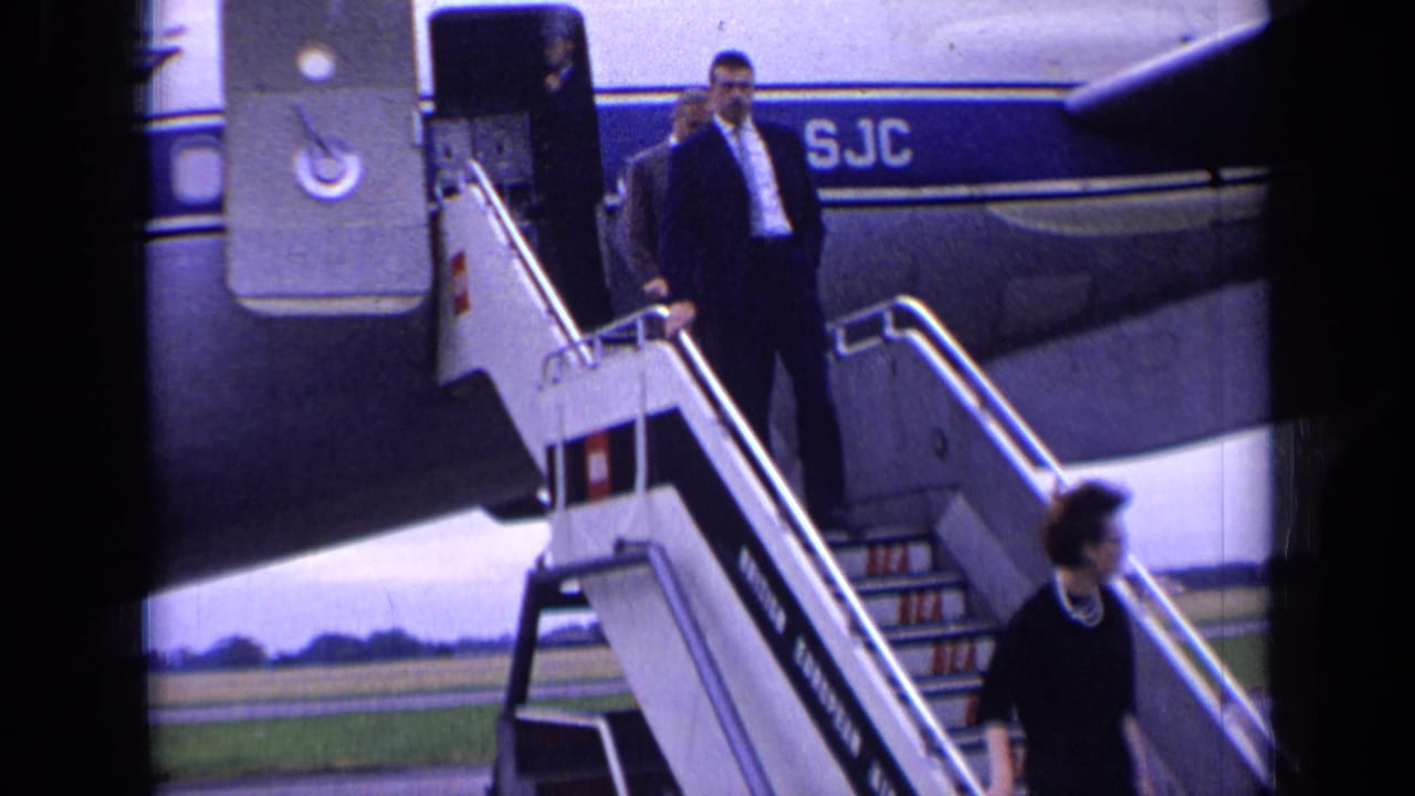 A suited passenger walks down mobile stairs from a blue-striped Boeing 707 during the London airport arrival scene.