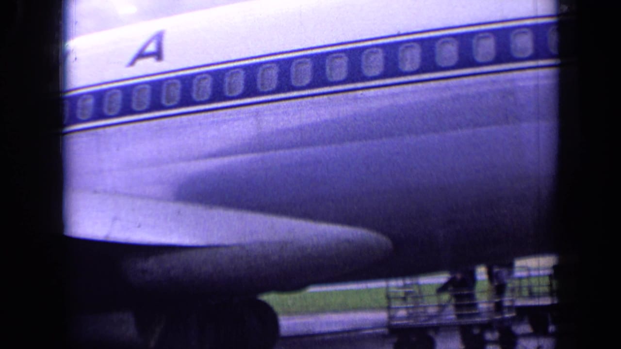 Sabena aircraft side with large letter A, passenger windows, wing root, tarmac, and service platform below.