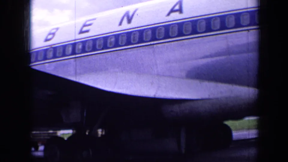 1963 London airport home-movie frame with Sabena fuselage lettering, rows of windows, wing shadow, landing gear area, and tarmac.