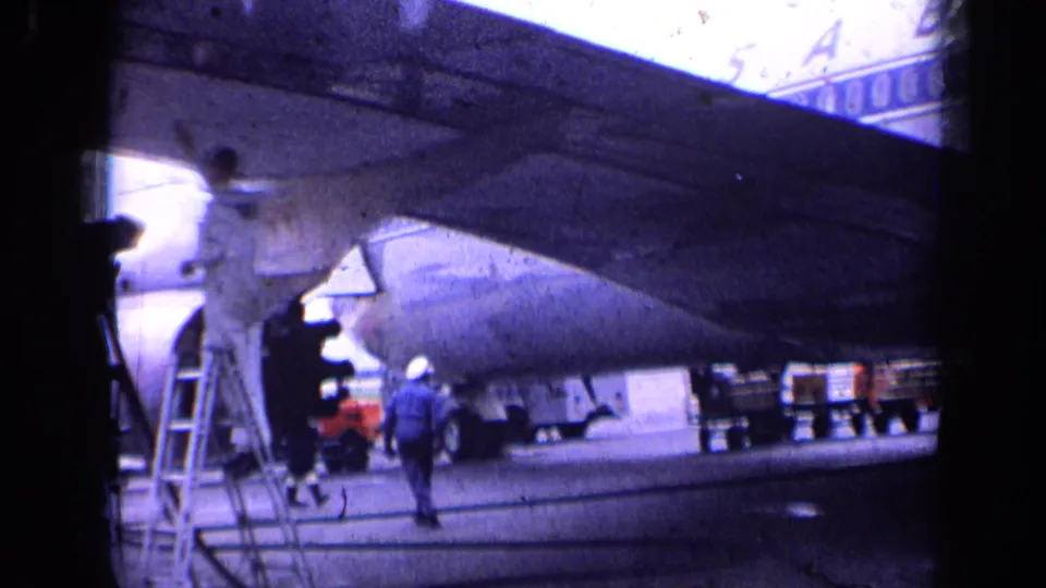 1963 London airport frame with workers, a service ladder, and ground support activity beneath a Sabena commercial airliner wing.