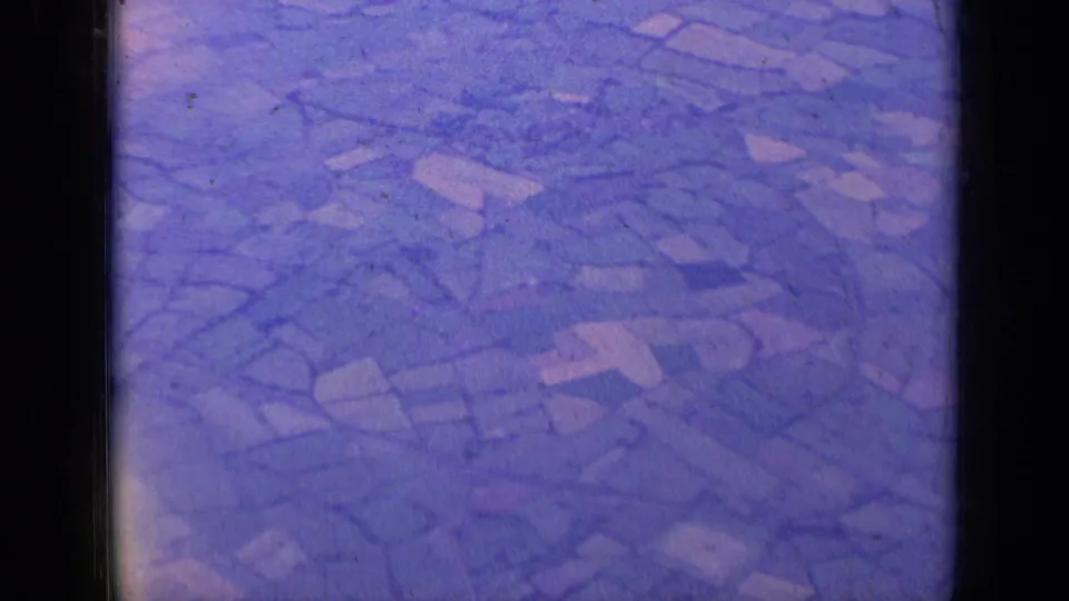 In-flight 8mm view over patchwork fields, likely shot from a passenger aircraft after departure from London.