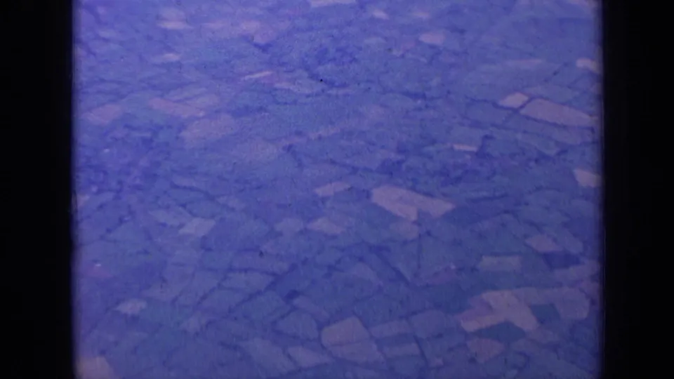1963 8mm aerial view near London showing patchwork fields and hedgerows with a blue-purple film cast.