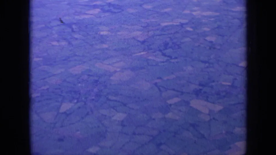 Aerial 8mm frame from 1963 near London with fields, hedgerows, and strong blue-purple aging of the film.