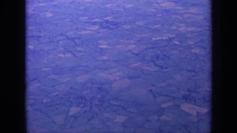 1963 London-area aerial home-movie frame showing rural fields and hedgerow divisions under a blue cast.