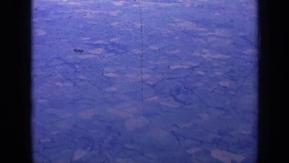 1963 8mm aerial view over rural England, showing patchwork fields and hedgerows through a blue-purple aged film cast.
