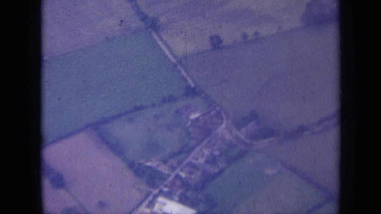 Aerial view of fields, lanes, and a small village cluster below.