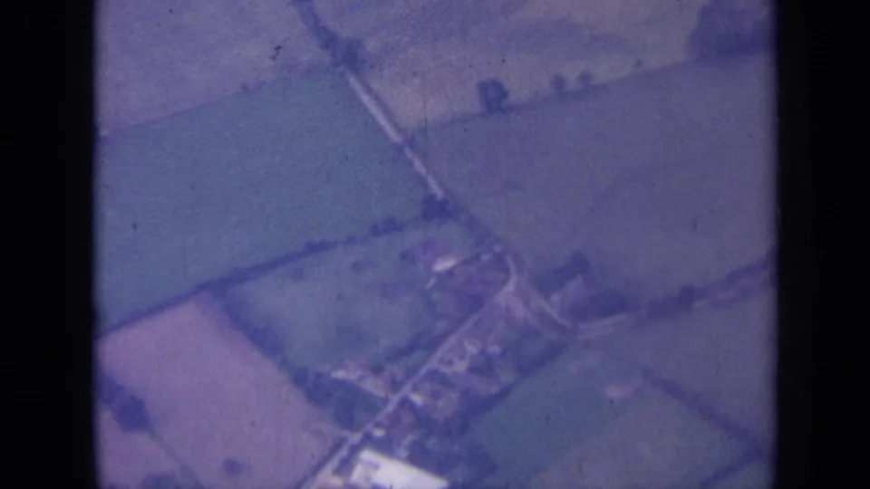 Aerial 8mm frame from rural England showing a small village or farm cluster among fields and narrow roads.