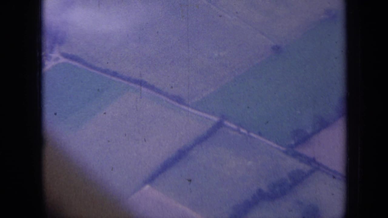 1963 8mm aerial view near London, England, showing patchwork farmland divided by hedgerows through a dark window frame.