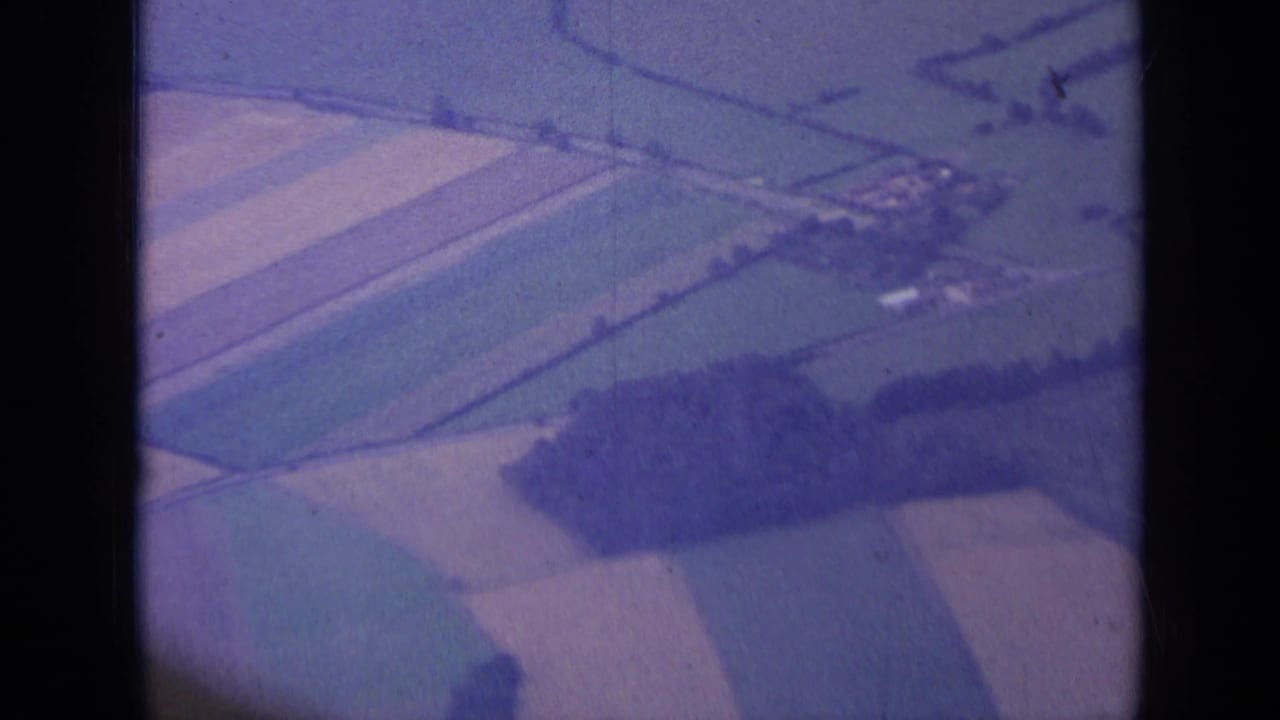Aerial 8mm view near London in 1963, showing farmland parcels, hedgerows, tree belts, and a small rural building cluster.