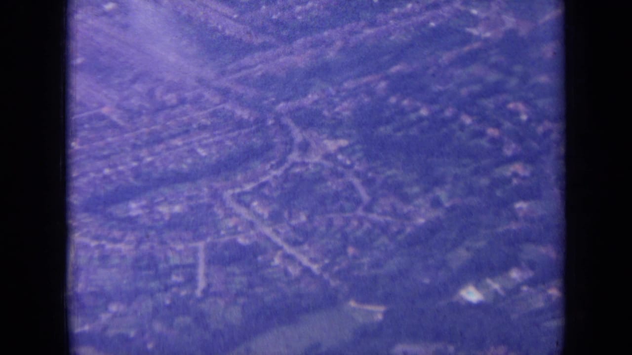 Clearer 1963 8mm overhead view of suburban London streets, housing blocks, trees, and open areas from an airplane.