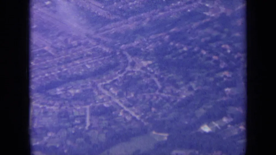 Clearer 1963 8mm overhead view of suburban London streets, housing blocks, trees, and open areas from an airplane.