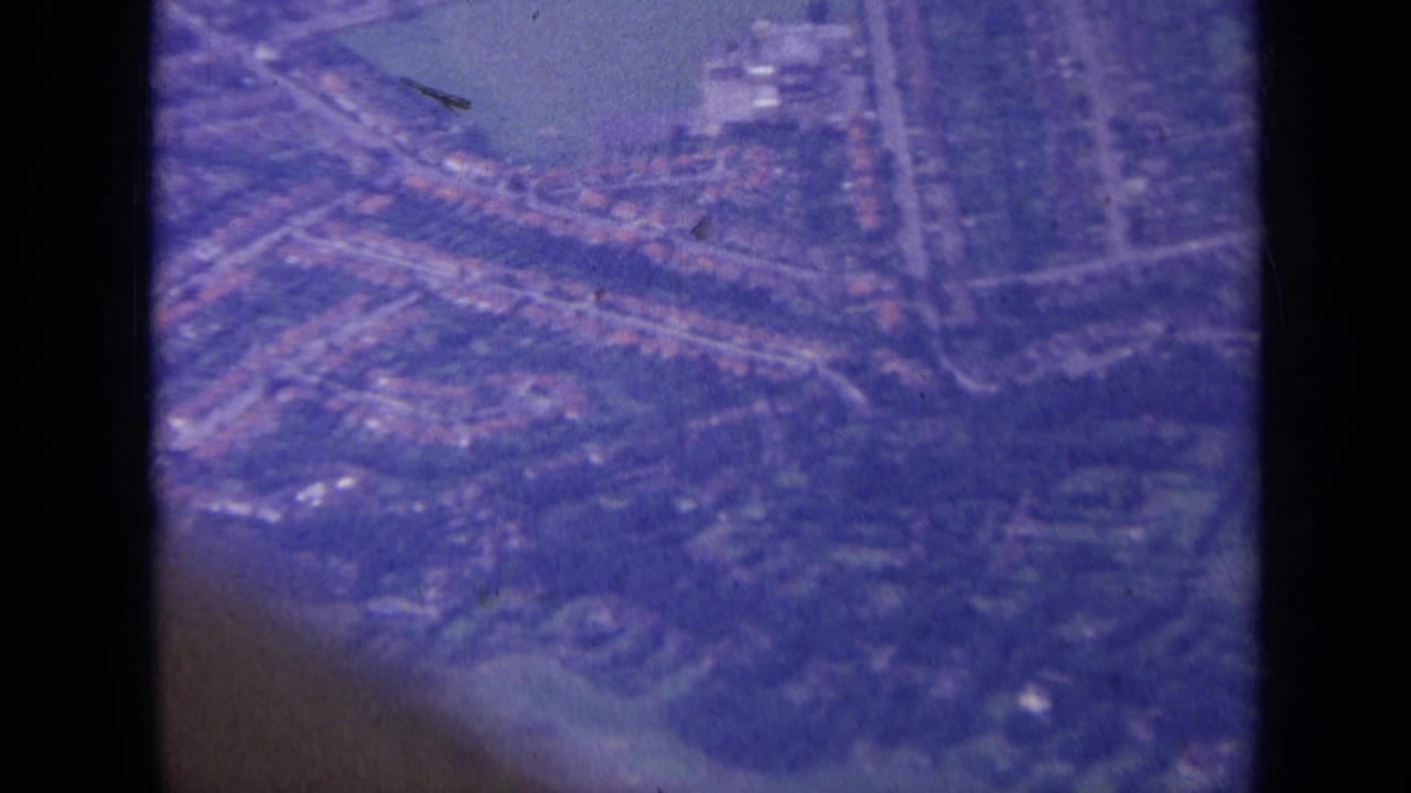 Aerial view of suburban streets and houses seen through a dark aircraft-window edge.
