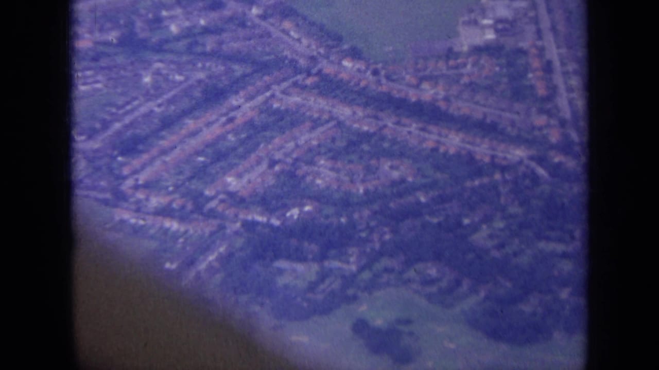 Suburban neighborhood from above with roads, houses, fields, and dark vertical window framing.