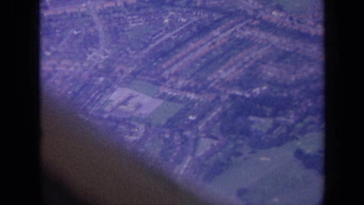 London suburban landscape from above in 1963, showing houses, roads, playing fields, and water through an aircraft window.