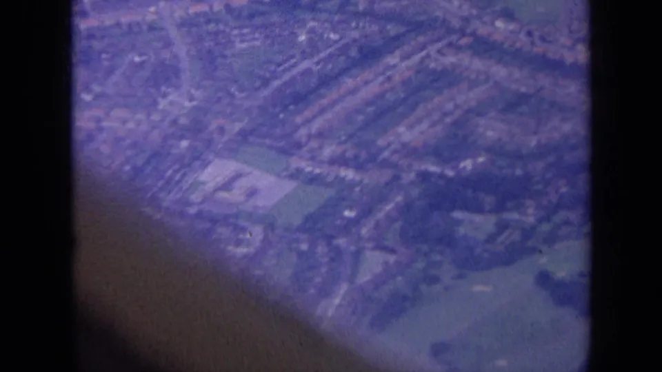 London suburban landscape from above in 1963, showing houses, roads, playing fields, and water through an aircraft window.
