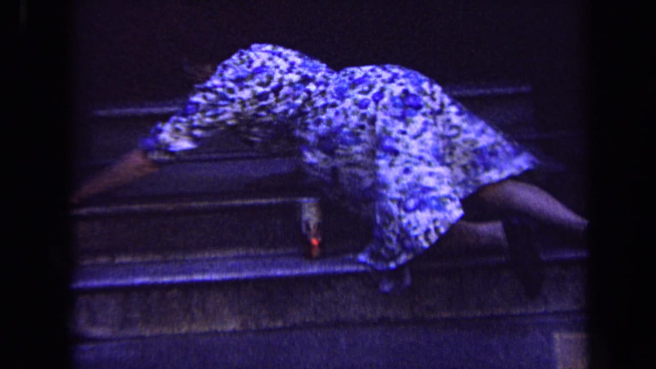 A woman in a floral dress leans across the stone steps, partly obscured by low light and strong blue film color.