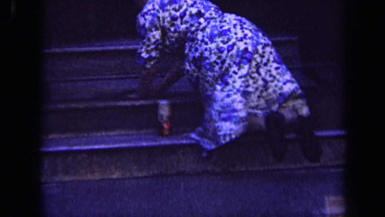 The woman bends near the stone steps, with her floral dress prominent in the blue-shifted 8mm frame.