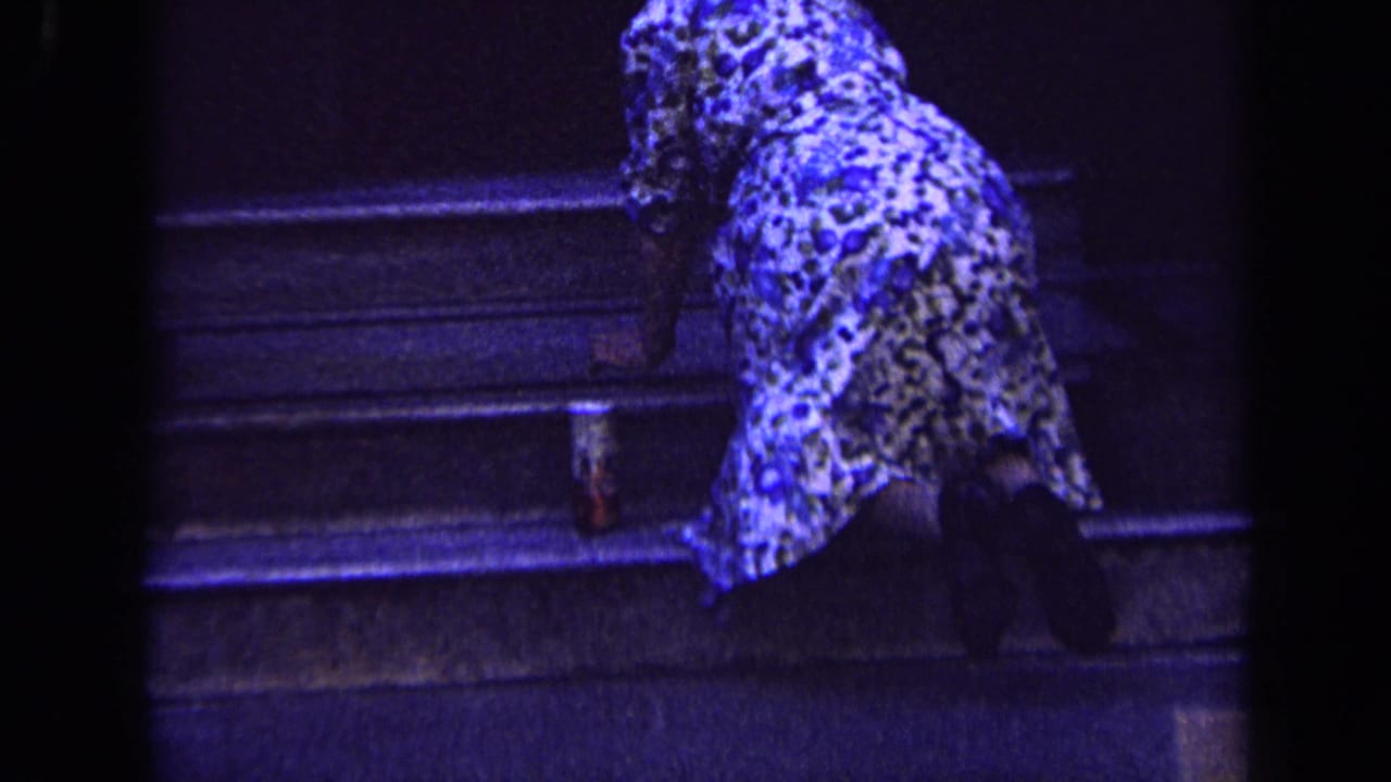 Woman in patterned clothing kneels on dark stone steps while cleaning near a small container.