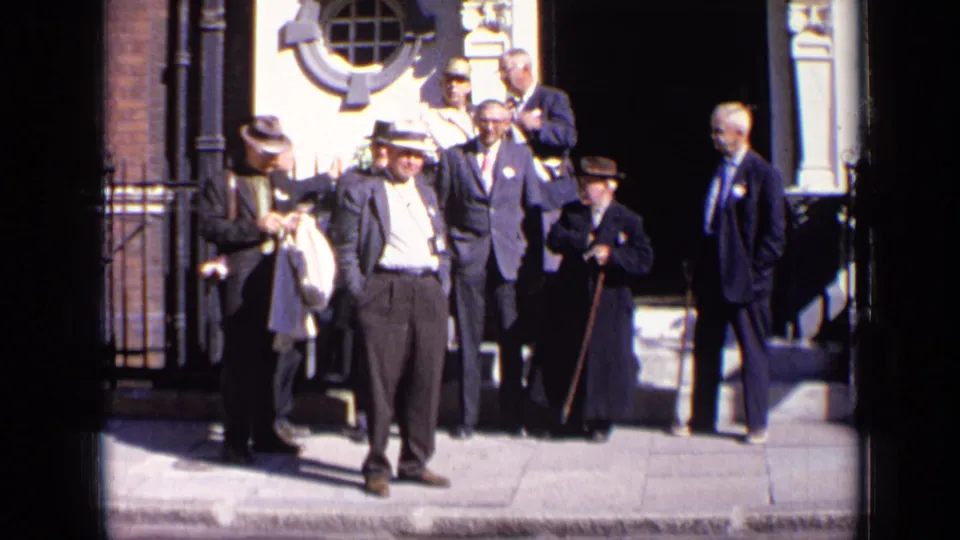 In the final frame, suited men and hat-wearing figures stand near a London doorway, several faces visible in the bright street light.