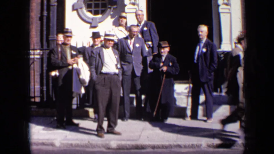 The group of suited men remains outside the ornate London facade while a blurred pedestrian moves at the edge of the frame.