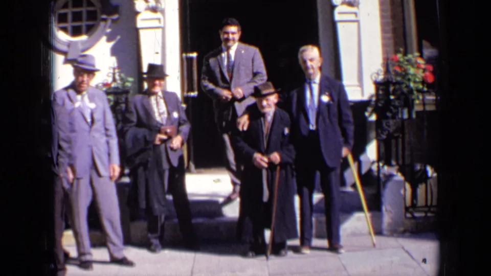 Five formally dressed adult men stand on London steps in 1963, framed by railings, flowers, and an ornate entrance.