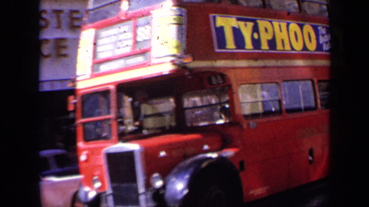 1963 London street view with a red double-decker bus carrying a large Ty-Phoo tea advertisement and blurred shopfronts behind it.