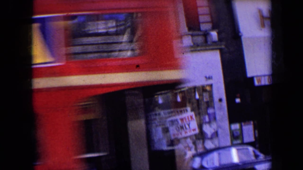 Blurred red double-decker bus moving past storefronts on a city street.
