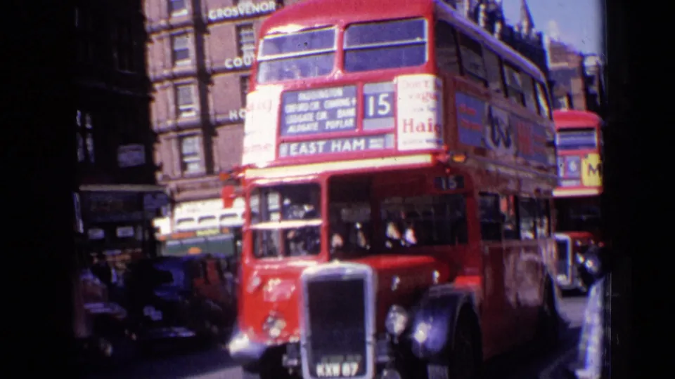1963 London view of a route 15 red double-decker bus with destination boards, surrounding buildings, and vehicles nearby.